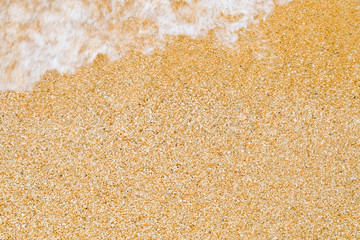 Background and texture of coarse sea sand with a wave, running from top left out of focus.