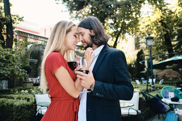 Beautiful romantic couple with glasses of wine happily hugging on date in restaurant outdoor