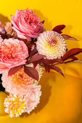 Floral composition of dahlia flowers, roses and autumn leaves. Arty, bright red and pink color  bouquet of flowers on yellow background 