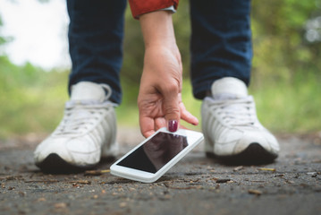 Woman picking up lost mobile phone from the ground.
