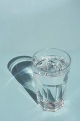 A glass of pure water under sunlight with deep stylish shadows on blue background copy space