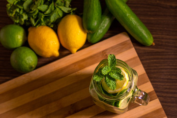 Infused water on a glass surrounded by its ingredients.- Detox water mix of cucumber, lemon, lime and mint.