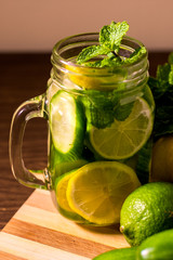 Infused water on a glass surrounded by its ingredients.- Detox water mix of cucumber, lemon, lime and mint.