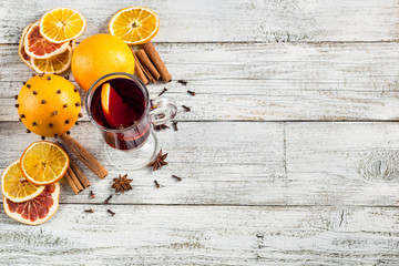 Glass of delicious mulled wine with oranges anise cinnamon on white wooden table