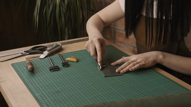 Female worker of leather draws line for holes by pressing with special tool. Process of manufacturing leather wallet handmade. Handmade leather goods