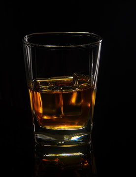 Glass of whiskey with ice on a black background with reflection.