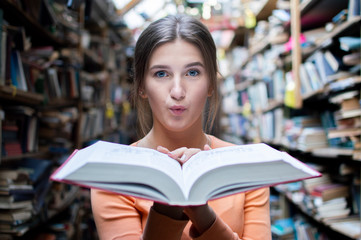 girl student reads a big old book in the library and blows dust, close-up