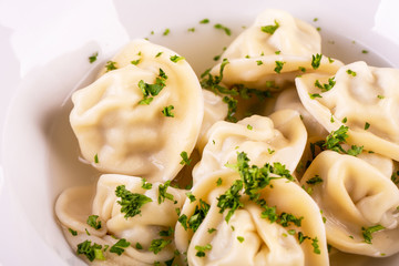 Beef pelmeni in broth, are served with greens and sour cream