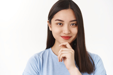 Unaltered motivated smart assertive asian girl acne prone skin pimples forehead smiling delighted touch chin ponder interesting suggestion thoughtfully accept offer, thinking white background