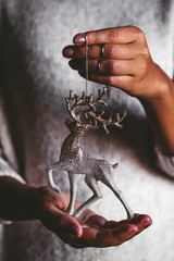 Woman in warm sweater holding toy deer glass decorative ball in hands, copy space. Christmas, new year holiday celebration concept