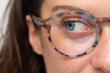 close up on Veins of the eye on young girl blue eye wearing with corrective lens glasses, looking side