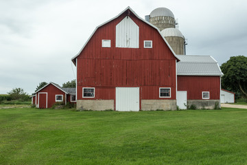 Multistory red barn with silos on green grass with an overcast sky © Richard