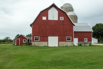 Multistory red barn with silos on green grass with an overcast sky