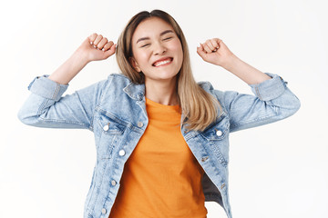 Obraz na płótnie Canvas Yes such lucky beautiful sunny summer day. Charming cheerful beautiful asian blond girl stretching raise arms up close eyes smiling broadly delighted triumphing perfect weekends, white background
