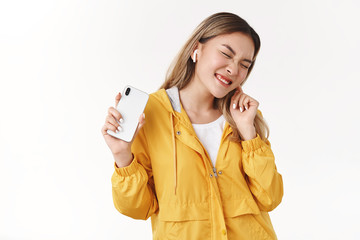 Yeah juicy beats. Cheerful carefree joyful good-looking modern asian blond girl wrinkle nose delighted close eyes smiling touch wireless earphone hold smartphone listen awesome music enjoy songs