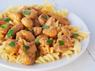 Creamy chicken stroganoff with fusilly pasta on plate over white wooden table