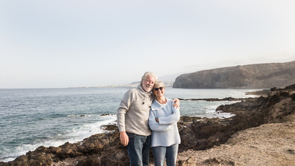 Two happy senior people standing on the cliff of the ocean.Hugging and smiling. Morning soon outdoor with clear sky. Vacation and happiness for pensioners