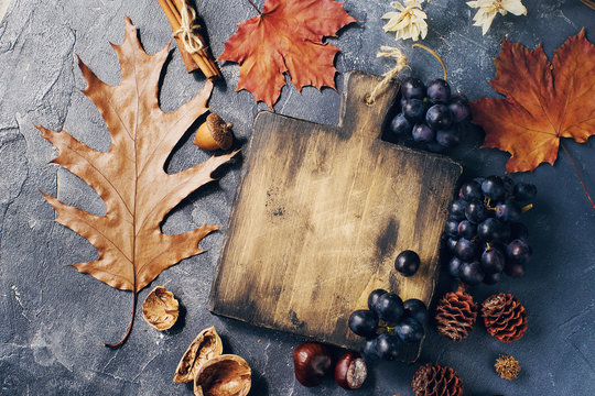 Autumn composition with cutting wooden board, marple leaves, freshly harvested ripe grapes, cones and wallnuts on dark stone table © Irina