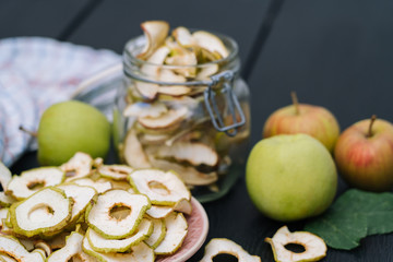 Dried apple slices in open glass jar. Homemade organic dried apple chips with fresh apple on black table background. Sweet vegan snack. Healthy and nutrition concept. Shallow depth of field. 