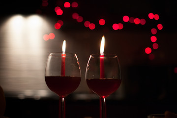 Romantic dinner: two glasses of wine and candels are in the dark with new year lights at the background