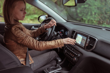 Fototapeta na wymiar Woman girl car interior leather jacket in autumn and spring, in forest park, chooses navigation touch screen, satellite internet application. Lost search of route, parking in fresh air rest in forest.