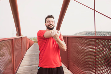 Sports mid adult man warming on a bridge after running