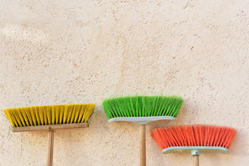 Three used plastic red broom leans with bristles facing up on a plastered wall with text box