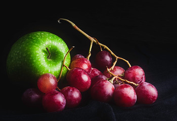 MANZANA VERDE CON RACIMO DE UVAS TINTAS SOBRE FONDO OSCURO. FRUTA SALUDABLE