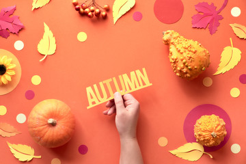Female hand holding text "Autumn, various paper leaves and Fall decorations on orange paper