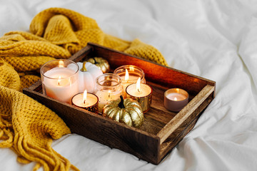 Burning candles pumpkin decoration on wooden tray with warm plaid in bed. Autumn style. Hygge...