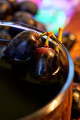 Black and red grapes in a glass with homemade wine, juice or alcohol tincture against the background of multi-colored festive lights. Farm harvest on the counter of the fair. Autumn still life.