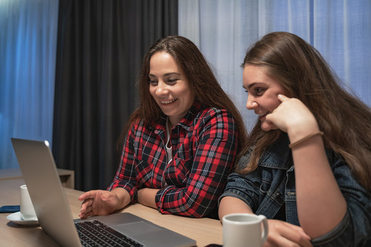 Two young girls or women laughing and discussing something using laptop, female lesbian couple spend time together