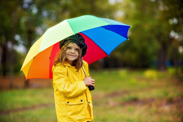 Happy funny child girl with multicolor umbrella in rubber boots at autumn park