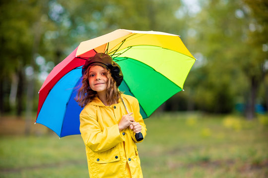 Happy funny child girl with multicolor umbrella in rubber boots at autumn park