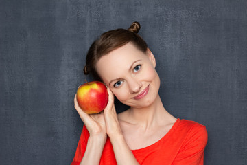 Portrait of happy young woman holding ripe apple near head