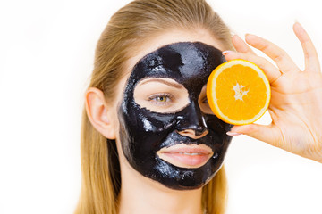 Girl black carbo mask on face holds orange fruit