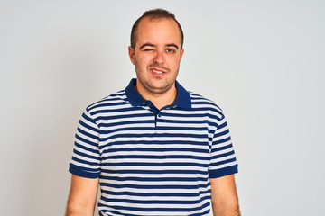 Fototapeta premium Young man wearing casual striped polo standing over isolated white background winking looking at the camera with sexy expression, cheerful and happy face.