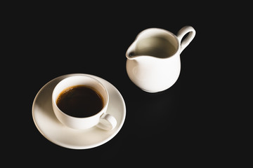 White espresso cup with coffee and milk jug on black background. Coffee cup rear view