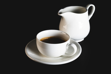 White espresso cup with coffee and milk jug on black background. Coffee cup rear view