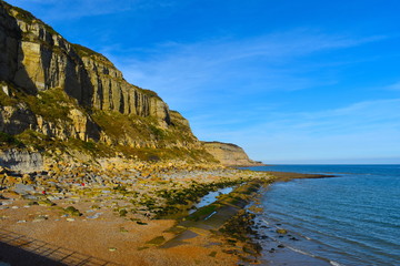 Fototapeta na wymiar The dramatic south coast of England. Cliffs, shingle beach and crystal clear sea on a bright sunny day. Hastings, Sussex county, South East England