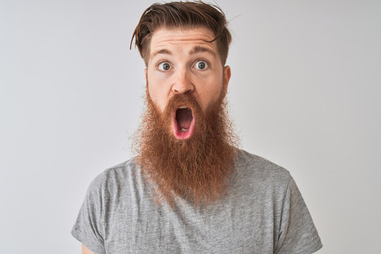 Young redhead irish man wearing t-shirt standing over isolated grey background scared in shock with a surprise face, afraid and excited with fear expression