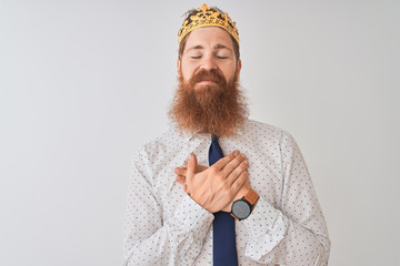 Young redhead irish businessman wearing crown king over isolated white background smiling with...