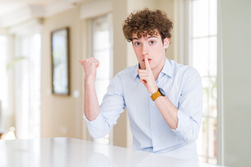 Young business man with curly read head asking to be quiet with finger on lips pointing with hand...