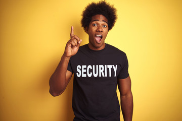 American safeguard man with afro hair wearing security uniform over isolated yellow background...