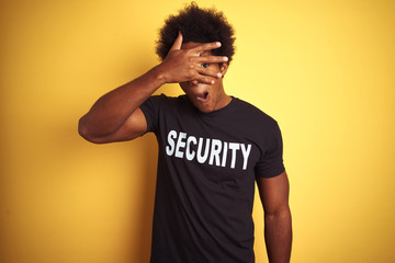 American safeguard man with afro hair wearing security uniform over isolated yellow background...
