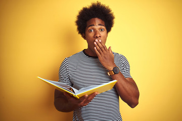 Afro american student man reading book standing over isolated yellow background cover mouth with...