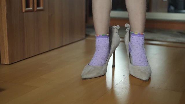 Child girl dresses adult shoes at home. Baby legs in socks and mother's shoe with heel