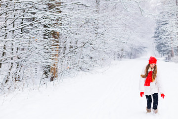 A girl with long hair in winter clothes have fun in the winter park among the snow-covered trees.