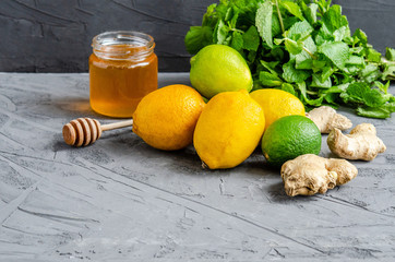 Citrus fruits lemons and lime, ginger root, mint leaves, fresh honey in a jar on a dark background. © Anna Tolstopiatykh