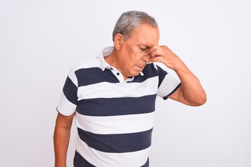 Senior grey-haired man wearing casual striped polo standing over isolated white background tired rubbing nose and eyes feeling fatigue and headache. Stress and frustration concept.